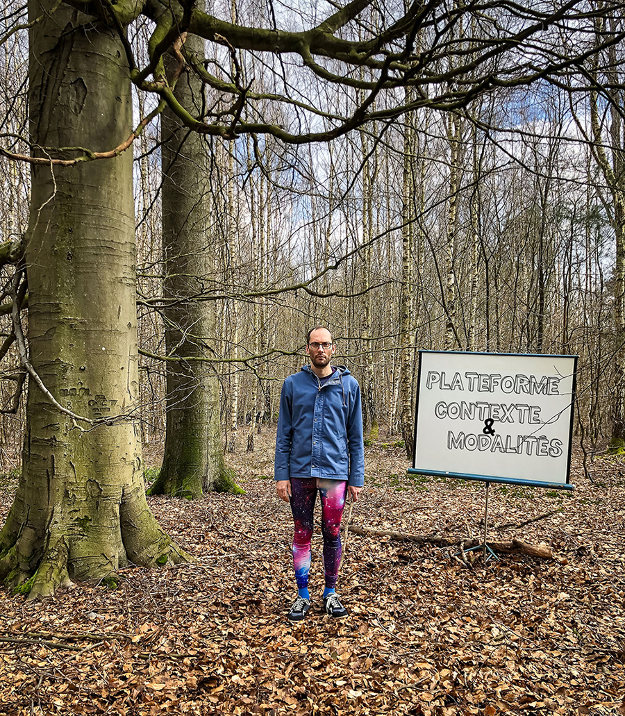 Antoine in the forest standing up next to a screen where it reads CONTEXT AND MODALITIES PLATFORM 