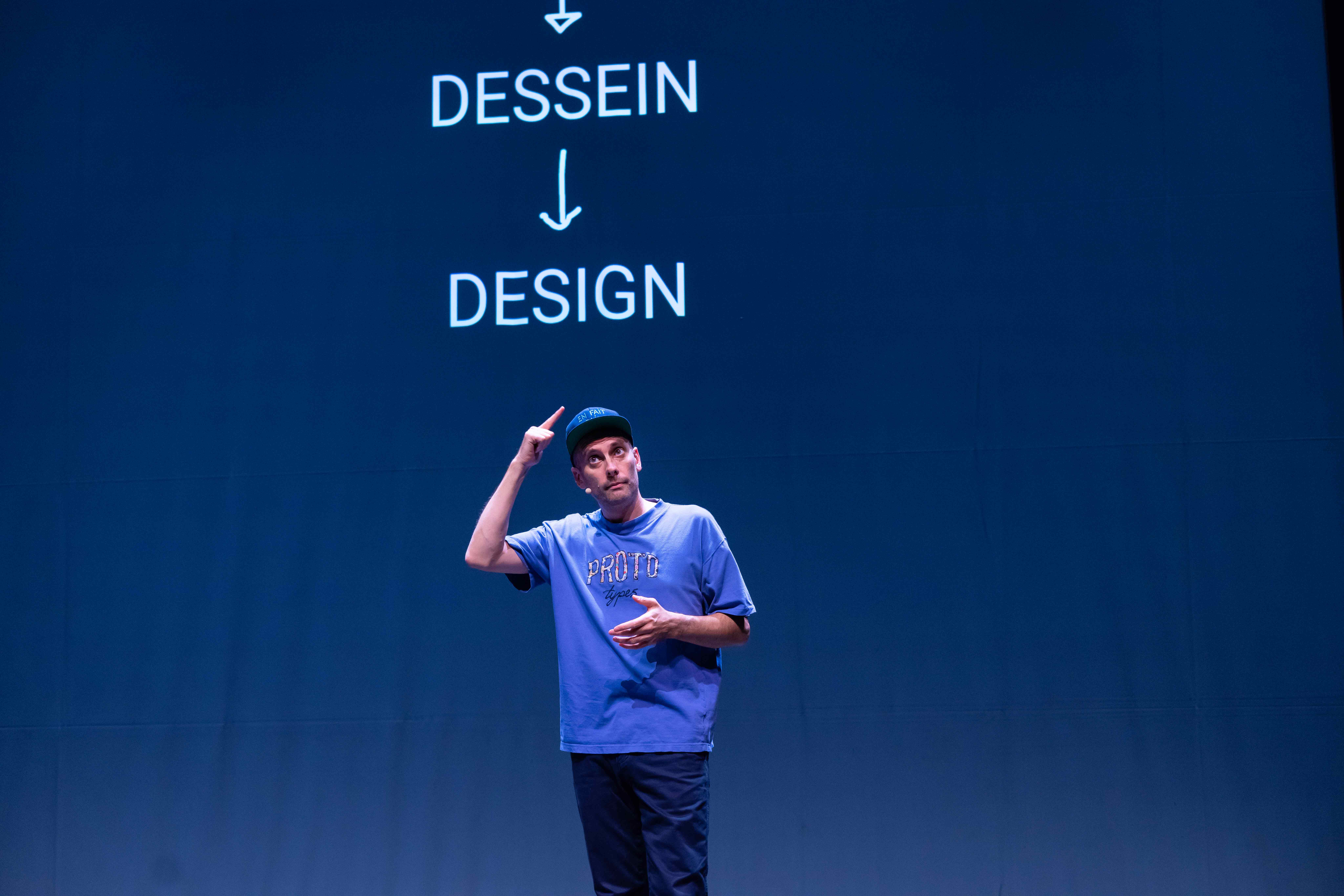 Antoine Defoort montre sa casquette en dessous d'une projection d'un schéma où on peut lire la filiation entre le mot dessein et le mot design
